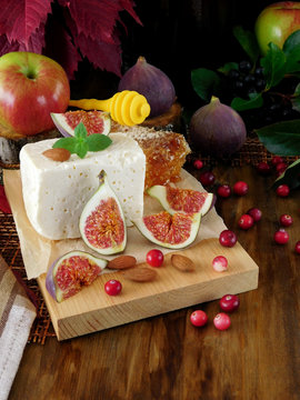 Cheese made of sheep milk and slices of figs on a wooden board surrounded by cranberries and almond. Ingredients for a cheese plate