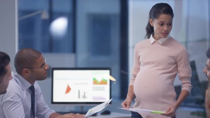  Pregnant businesswoman in a meeting with colleagues discussing financial data