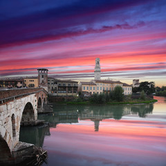 Roman empire ancient bridge Ponte Pietra over the river Adige in Verona, Italy during sunset with illuminated old town