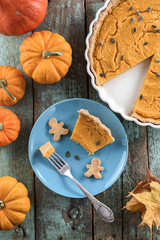 Healthy Thanksgiving dessert. Traditional pumpkin pie with wholegrain crust and pumpkin seeds served with gingerbread man cookies on blue plate decorated with small pumpkins