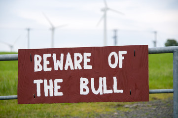 Beware of the Bull sign on a gate, with a windfarm in the background