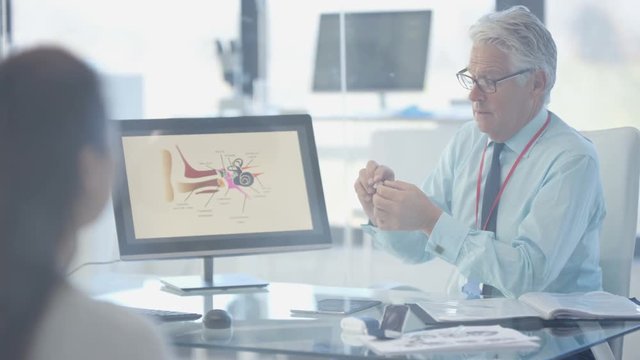  Audiology doctor showing patient a modern hi tech hearing aid & explaining