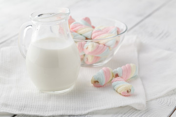 White and pink twisted marshmallows and a jug of milk on a white wooden table. Beautiful light background.
