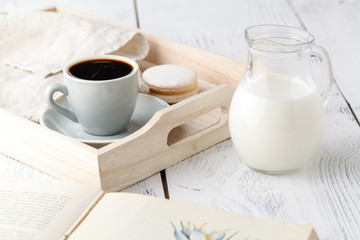 Cup of coffee and macaron cakes on tray on white wooden table