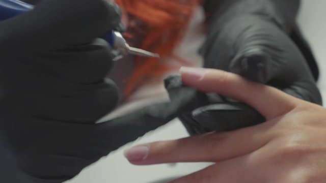 Manicurist is applying electric nail file drill to manicure on female fingers.