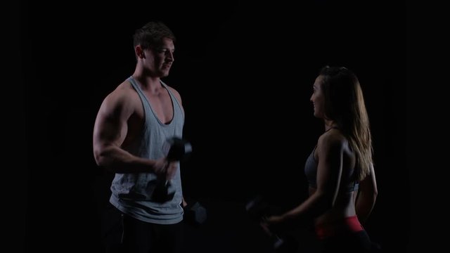  Fit young man & woman working out with weights against a black background