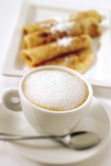 Cup of cappuccino, blurred crepes in background