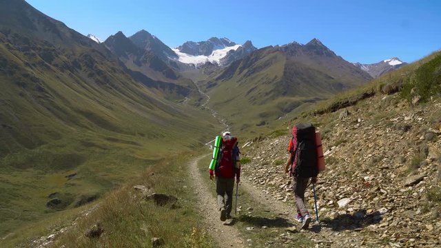 Two friends are hiking by the road in Caucasus mountains. Friends are walking in mountains 4K UHD