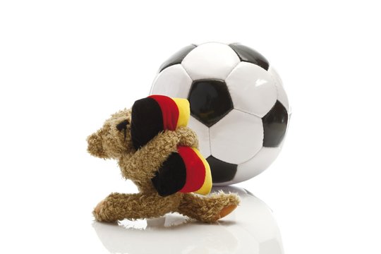 Teddy bear holding a cushion in the colours of the German flag standing in front of a football