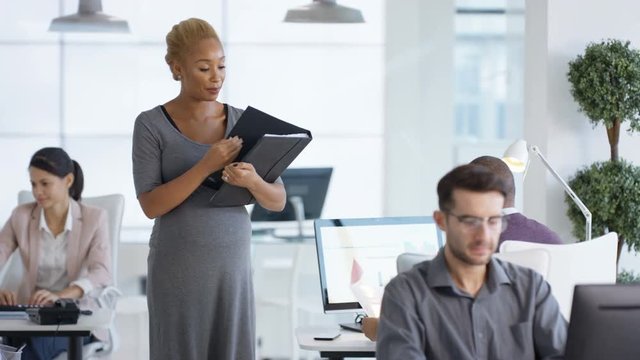  Pregnant businesswoman handing out paperwork to her colleagues in office