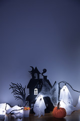 Halloween scene with a haunted house and ghosts. A decorative pumpkin and corn candy in front. Dark copy space. 