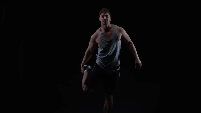  Fit young man with muscular physique stretching against black background