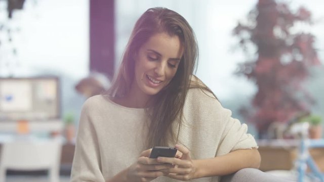  Attractive woman relaxing at home, smiling & texting on smartphone