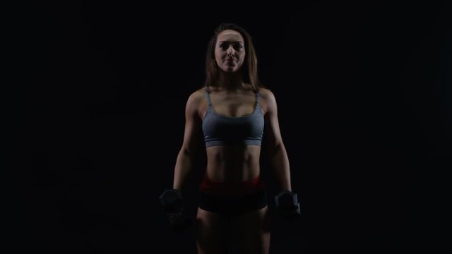  Fit woman with athletic physique lifting weights against black background
