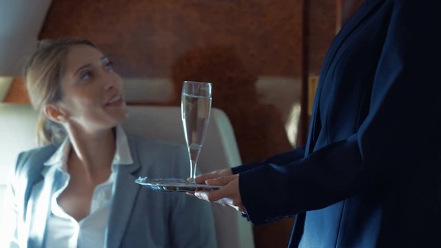  Air hostess serves champagne to businesswoman traveling on private plane