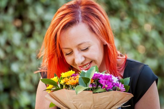A portrait of an elegant young Caucasian girl with red hair smiling and holding a flower bouquet in her hands, smelling the flowers. March 8, Valentine's Day concept, first date, wedding proposal.