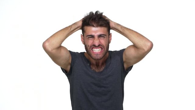 emotional skinny man with chest hair under grey t-shirt screaming in delight and excitement clenching fists touching head in shock over white background. Concept of emotions