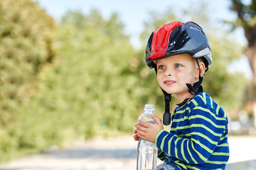 Fototapeta na wymiar Little boy drinking water by the bike