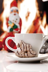 Coffee cup and a gingerbread cookie shaped as a little rocking horse, chimney fire and chocolate Santa at back