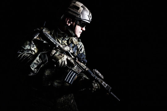 Half length low angle studio shot of special forces soldier in field uniforms with weapons, portrait on black background. Protective goggles glasses are on