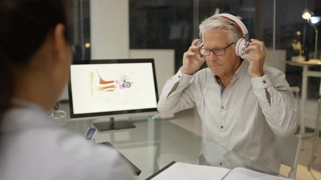  Mature man wearing headphones, getting a hearing test with audiology doctor. 