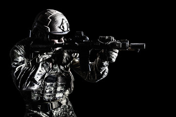 Half length low angle studio shot of special forces soldier in field uniforms with weapons, portrait on black background. Protective goggles glasses are on