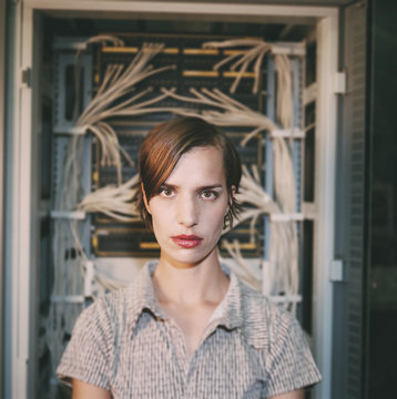 Portrait of young woman standing in front of computer servers and electrical wiring