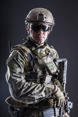 Half length studio shot of special forces soldier in field uniforms with weapons, portrait on black background. Protective goggles glasses are on