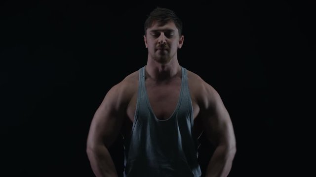  Fit young man with muscular physique lifting weights against black background