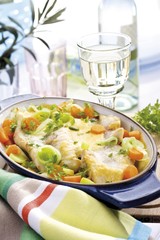 Fototapeta na wymiar Mediterranean seafood dish: ocean perch filets on a bed of vegetables scalloped with herbs and mustard sauce with a glass of white wine