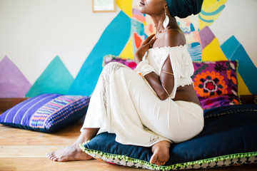 Young african woman sitting on the cushion floor in exotic colorful design space