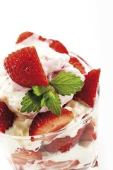 Whipped cream and strawberries garnished with mint leaves served in a parfait glass