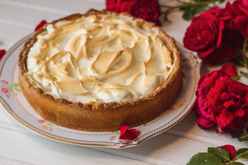 Meringue pie on a white table near red roses.