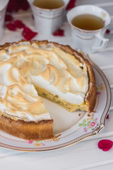 Pie with rhubarb and meringue  is cut on a white table near red roses and cups of tea.