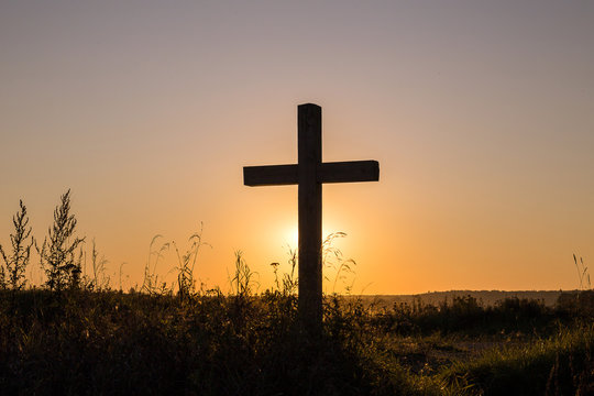 Wooden cross in the rural area against the background of a sunset in the summer