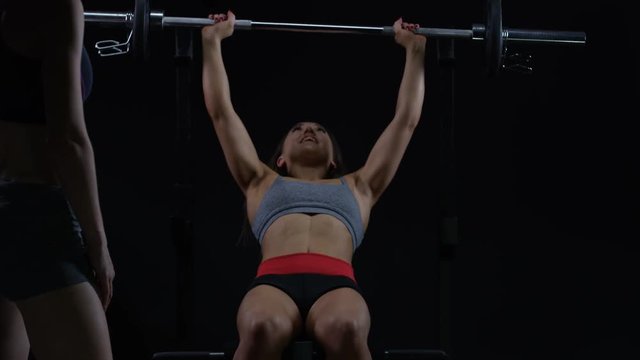  Fit young woman doing barbell bench press with personal trainer watching