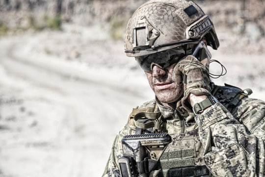 Closeup shot of soldier calliong phone in the desert among rocks