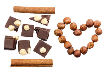 Pieces of bitter dark chocolate cubes with cinnamon stick and hazelnut in heart shape isolated on...