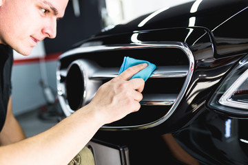Naklejka premium A man cleaning car with microfiber cloth, car detailing (or valeting) concept. Selective focus. 