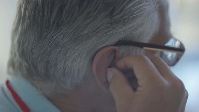  Close up of senior man putting a hearing aid into his ear
