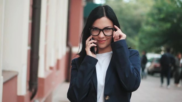 Businesswoman with smartphone close up. Girl speaks on cell phone. Beautiful woman in glasses talks on the mobile device, Female with white smartphone. Slow motion.