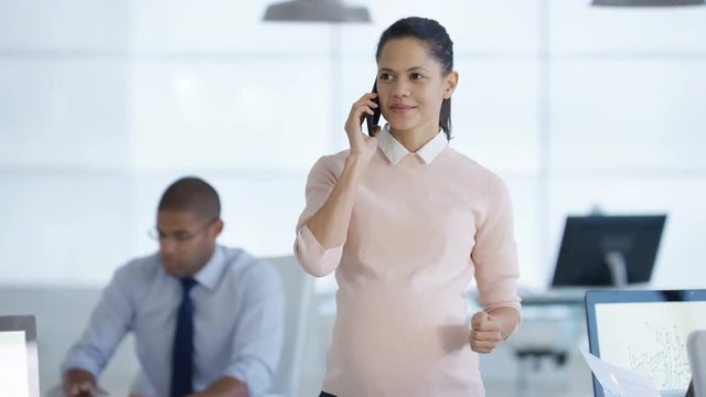  Pregnant business manager talking on the phone & overseeing staff in office