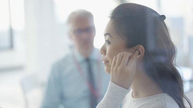  Woman with deafness being fitted for hi tec hearing aid doctor holding mirror