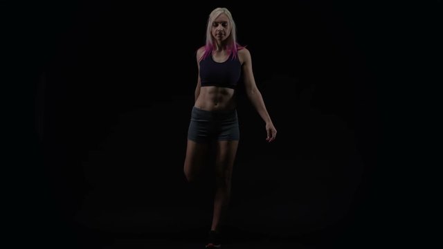  Fit young woman with athletic physique stretching against black background