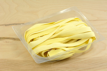 Fresh egg tagliatelle pasta noodles in opened plastic packaging on wooden table