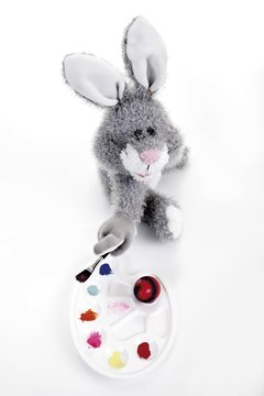 Easter bunny soft toy with palette of colors, paint brush and a coloured easter egg