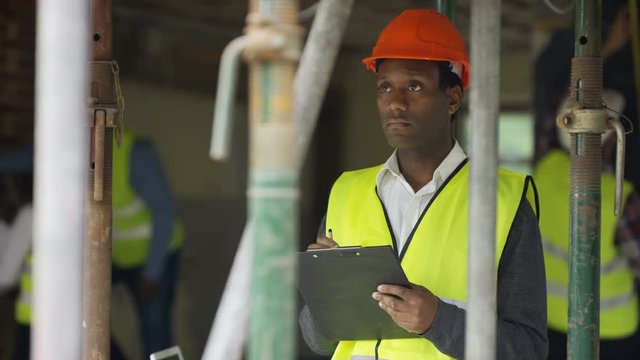  Portrait smiling worker at construction site writing notes on clipboard