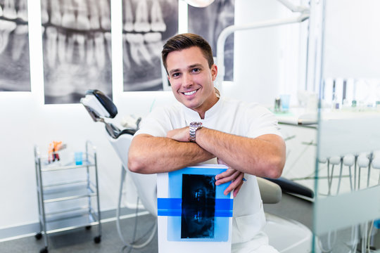 Portrait of handsome smiling dentist holding  x-ray image of his patient.