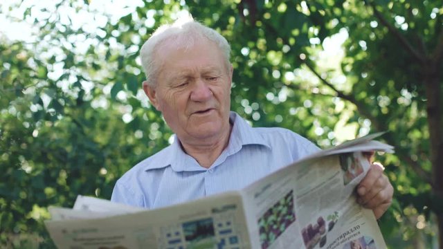 Handsome senior reading the newspaper in the garden. 4K