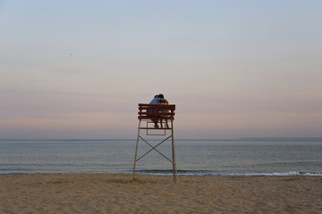Fototapeta na wymiar Loving couple sits in a lifeguards chair at sunset